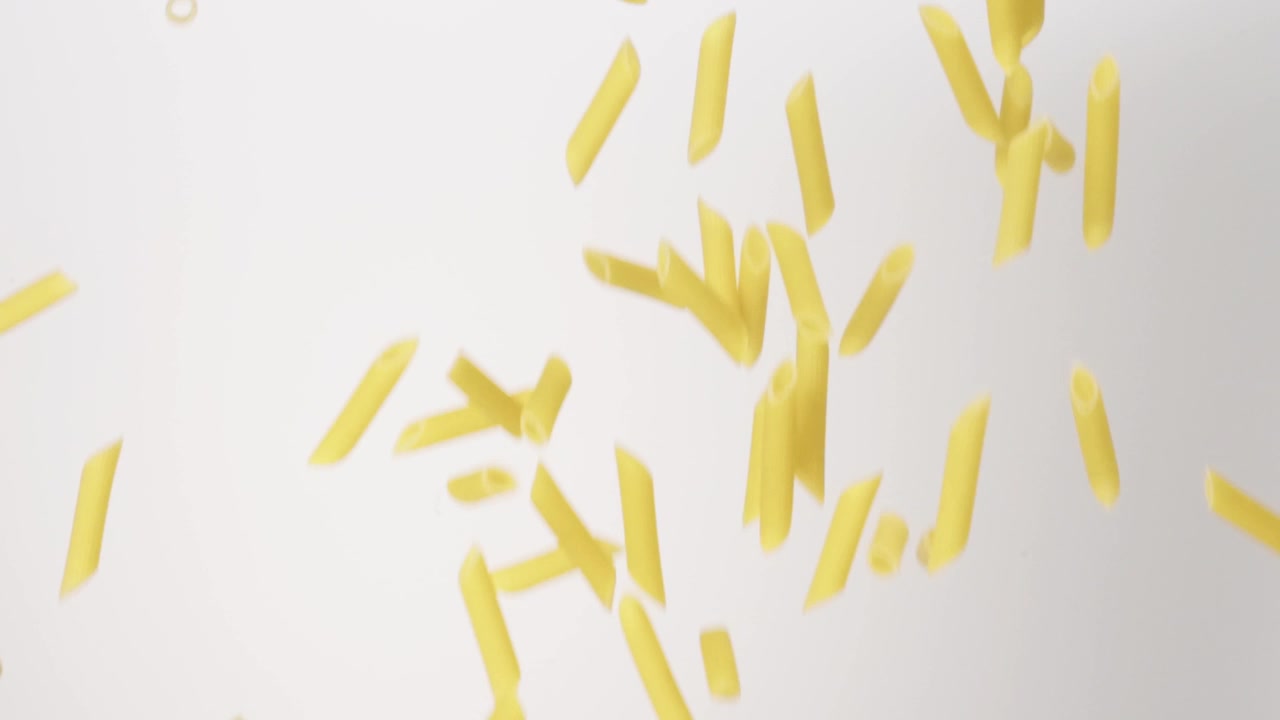 Penne secche non cotte che piovono su uno sfondo bianco in slow motion, primo piano macro