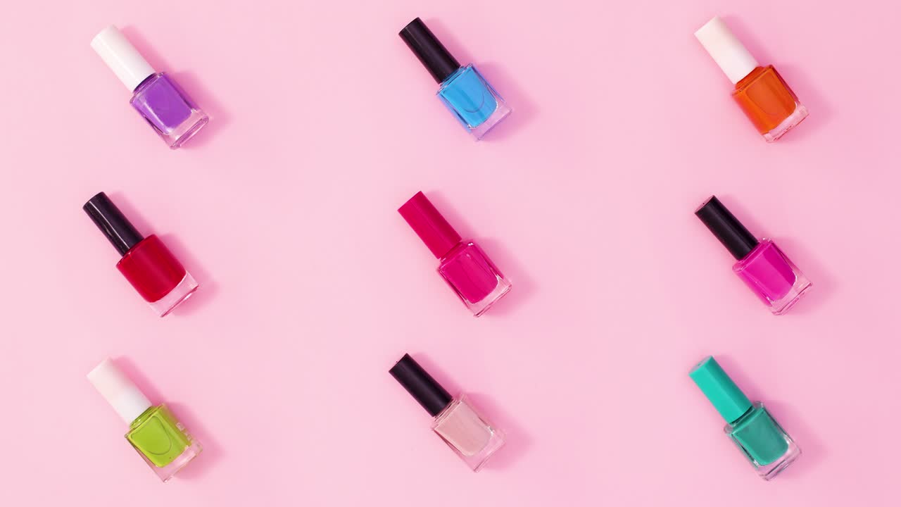 patrón creativo hecho de botellas de esmalte de uñas de manicura en diferentes colores girando sobre un fondo rosa pastel. detener el movimiento