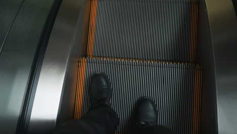 a black-booted leg on an escalator step. the camera captures the movement and texture of the escalator in a modern indoor setting, focusing on the foot and the steps