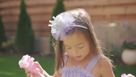 a little girl in a dress is blowing soap bubbles in the backyard on a sunny summer day