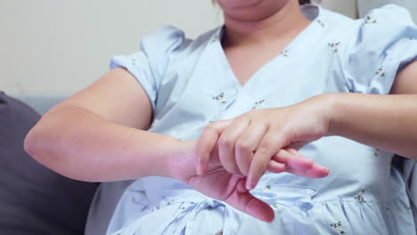 a pregnant woman putting pressure on her right arm by squeezing and pressing them down while she is sitting on her couch in the living room