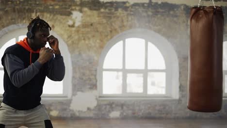 afro american young male boxer practicing shadow boxing in headphones in bright hall