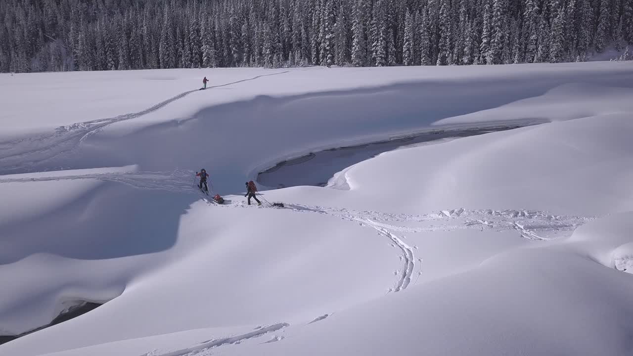 Advancing aerial: Expedition skiers with pulk sleds cross snowy river