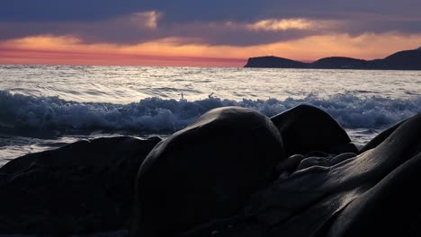 beautiful dreamy sunset with red sky and dark clouds reflecting on sea, waves splashing on illuminated cliffs