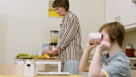 girl drinking juice and doing homework while her mother is doing smoothie with the blender