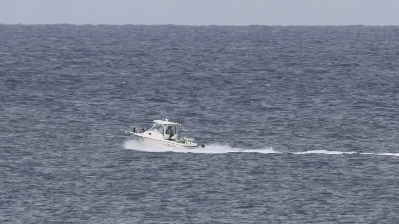 A white boat speeds across expansive ocean waters, leaving a trail of white wake behind.