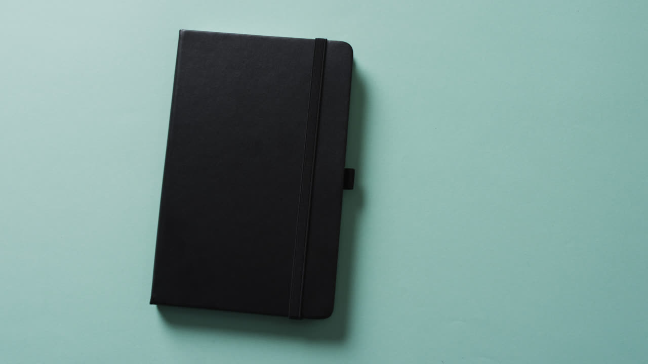 Close up of closed black notebook with copy space on green background in slow motion