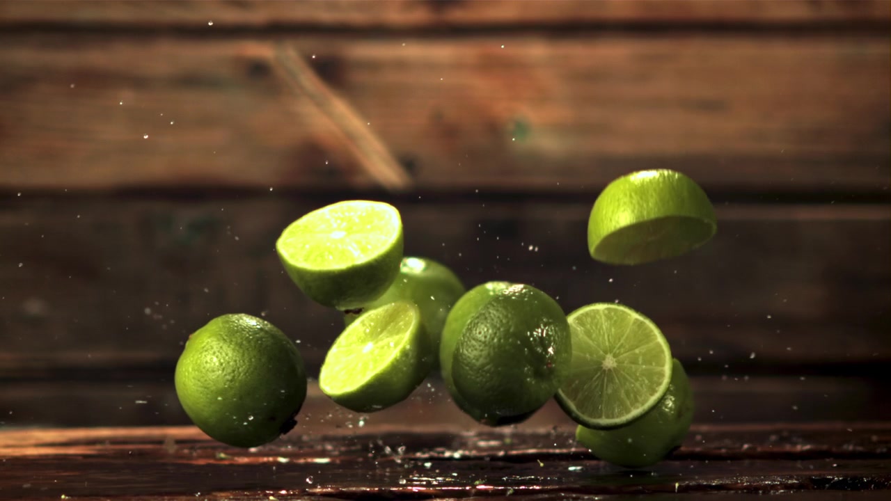 Fresh Limes and Slices Falling and Splashing Water on a Wet Wooden Surface