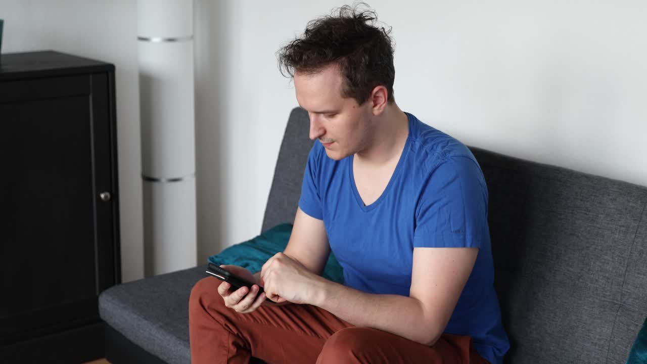 Man sitting on the sofa in the living room and watching on the smartphone