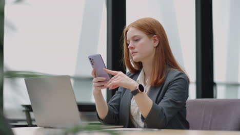 young businesswoman use smart phone with laptop. business woman in a modern office with a panoramic window sunny day laptop tablet use a mobile phone in a situation