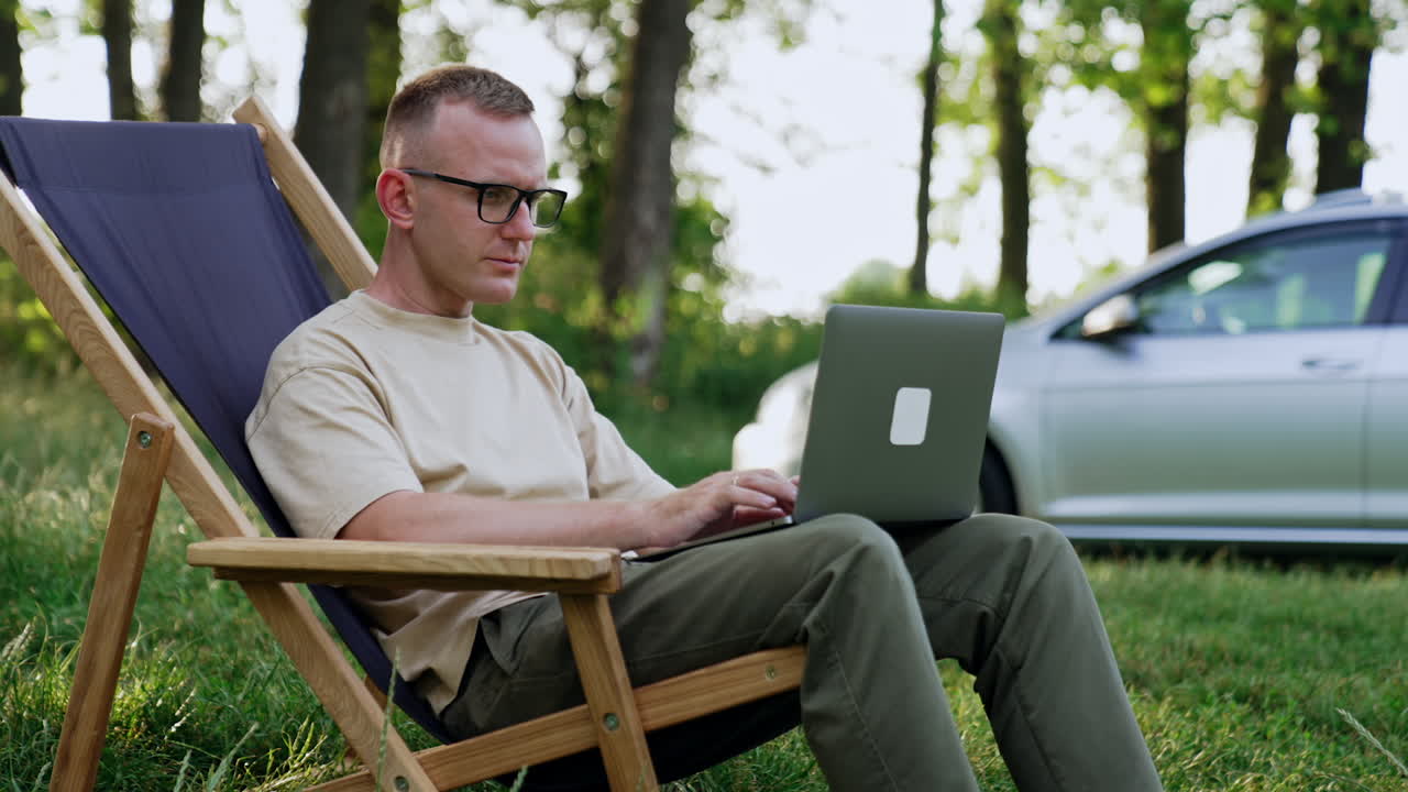 Focused man wearing glasses works on laptop. Businessman having trouble, puts off glasses and rubs his forehead. Close up.