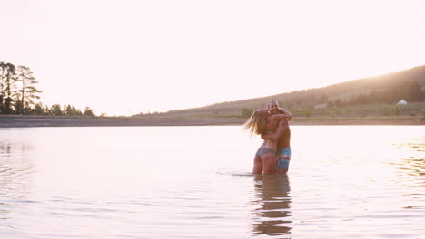 romantic couple splashing in lake backlit by evening sun