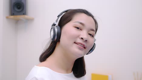 Asian-woman-smiling-using-the-bluetooth-headphone-for-listening-to-music-and-looking-at-the-camera-so-lovely-lie-in-bed