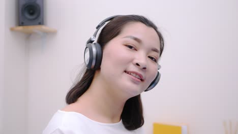 asian woman smiling using the bluetooth headphone for listening to music and looking at the camera so lovely lie in bed