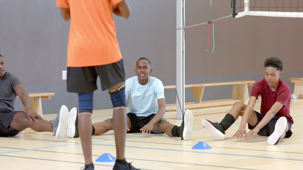 Diverse Teamkollegen folgen der Demonstration des Trainers und wärmen sich auf dem Sporthallenboden mit Hütchen und Netz auf.