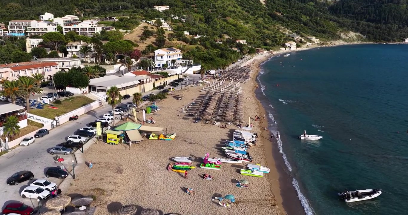 Vista aerea della spiaggia di Agios Georgios Pagon sull'isola di Corfù, Grecia, con sabbia dorata, acqua di mare turchese, ombrelloni e uno sfondo di rigogliose colline verdi
