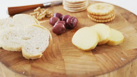 Slices-of-bread,-crackers,-olives,-walnut-and-knife-on-wooden-board