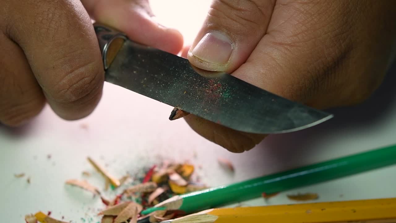 Opptak av hender som sakte spisser en blyant og noen fargeblyanter med en skarp kniv