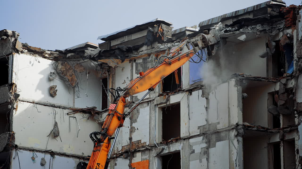 Tall building destroyed by an earthquake. Demolition machine tearing down roof of a wrecked building. Long machine claw pulling down the debris.