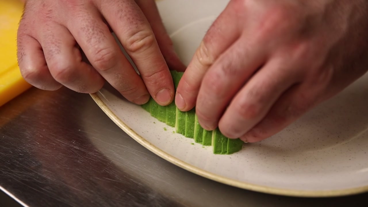 Hands Arranging Fresh Sliced Avocado on a White Plate