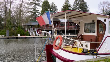 a narrowboat sits on the erdre river in france with a french flag waving on the back