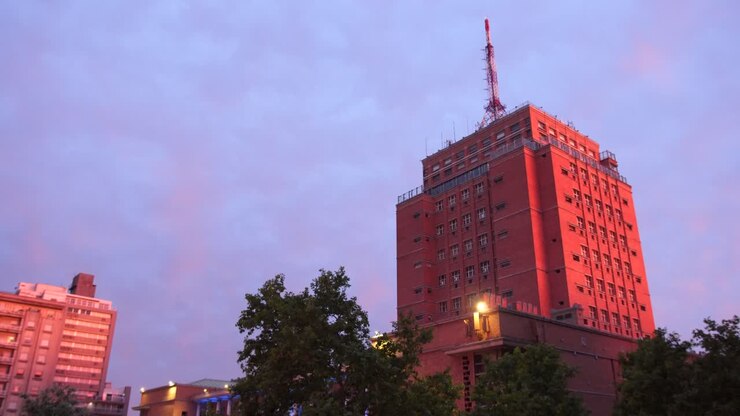 Intendência de Montevideo, Uruguai ao pôr do sol. Um grande edifício feito de tijolos com uma antena, céu azul com nuvens rosas