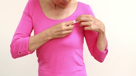 Smiling-woman-putting-pink-ribbon-on-shirt