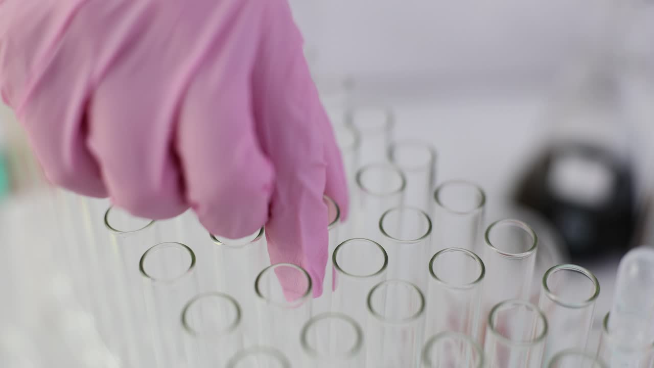 Gloved hand arranging test tubes in a laboratory