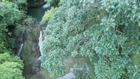 vista ascendente de drones de una mujer con un vestido rosa parada en la base de una cascada