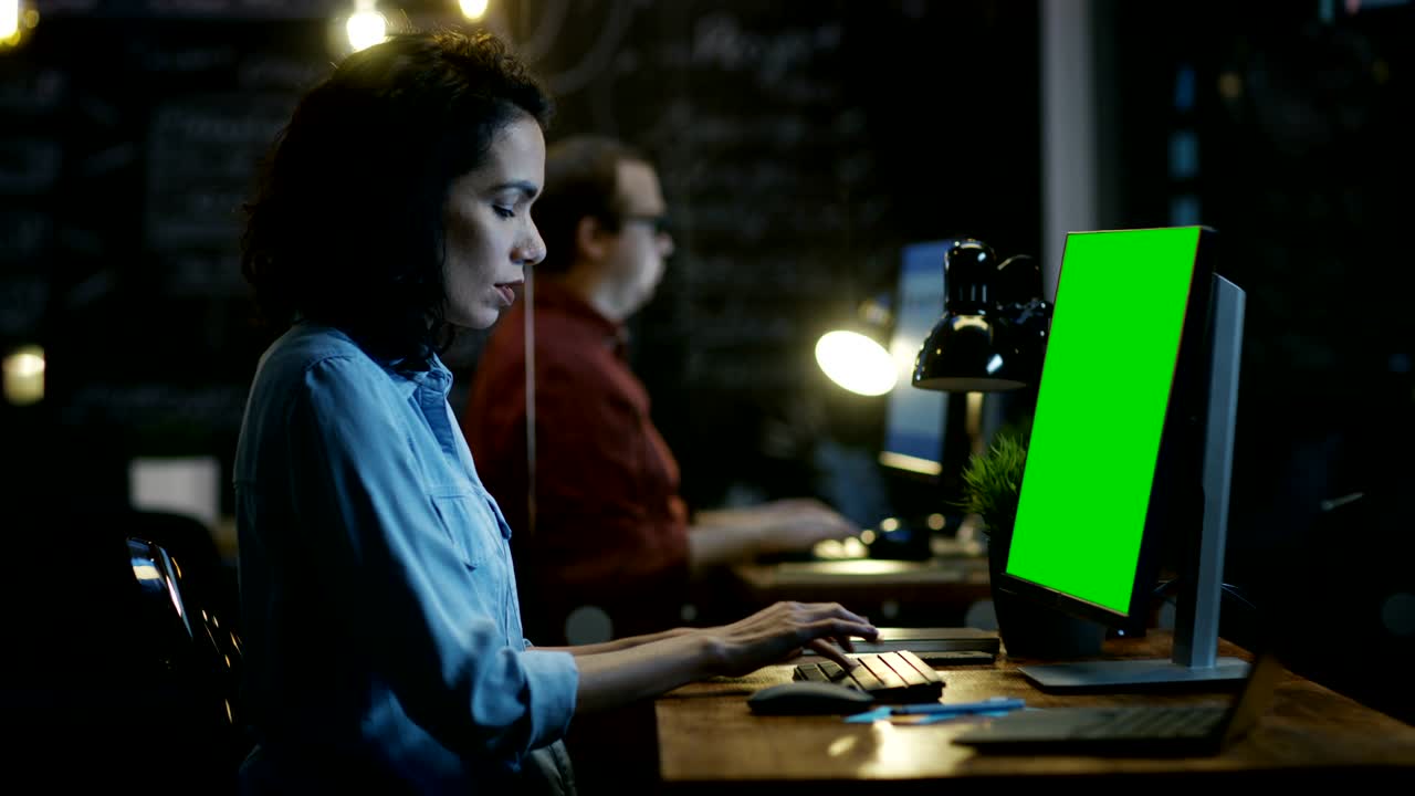 una empleada de oficina estresada y sobrecargada de trabajo sostiene la cabeza en las manos mientras trabaja en una computadora personal con una maqueta de pantalla verde. en el fondo de la oficina creativa.