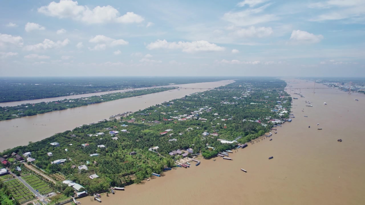 Un'avanzata di drone sul Delta del Mekong in Vietnam rivela una lunga isola popolata circondata da ampi canali fluviali fangosi, vegetazione tropicale, insediamenti rurali e imbarcazioni che navigano i corsi d'acqua.