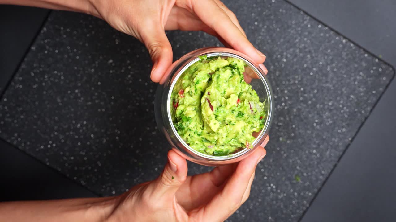 Detailní pohled na guacamole ve skleněné misce. Ruce drží skleněnou misku plnou čerstvého domácího guacamole.