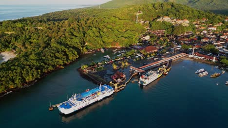 ferries waiting at padang bai port in bali as a drone view captures the calm sea, nearby boats, and green hills surrounding this active coastal gateway between islands.