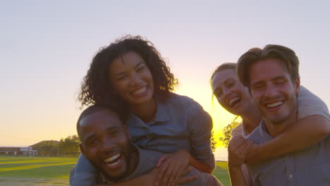 Two-smiling-couples-piggybacking-outdoors,-close-up