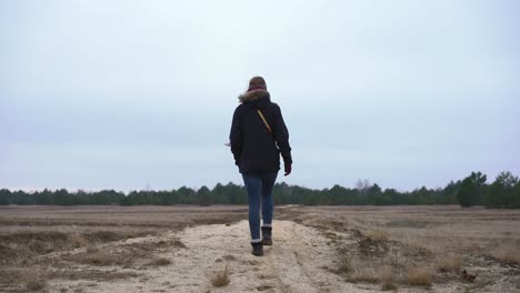 Female-hiker-walking-away-from-camera-in-countryside-field,-rear-view