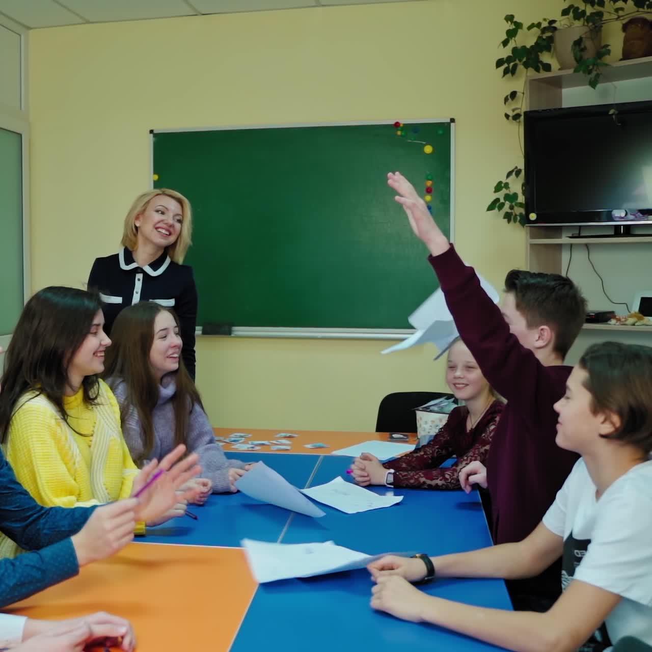 Group of students at school. Boy is throwing papers up. School children are sitting at one desk and enjoy time together. Education concept. Slow motion.