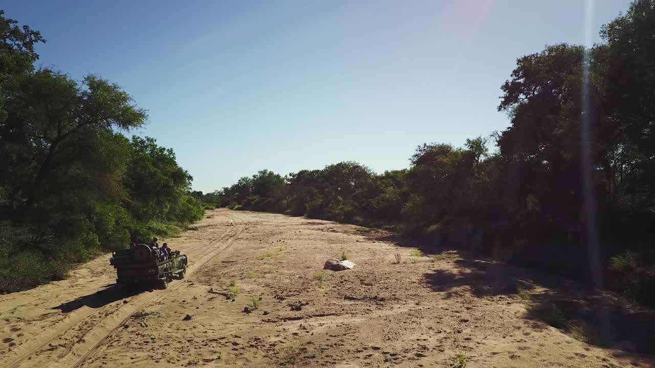 rastreando un vehículo de juego en un lecho de río seco en el calor del sol de la tarde africana