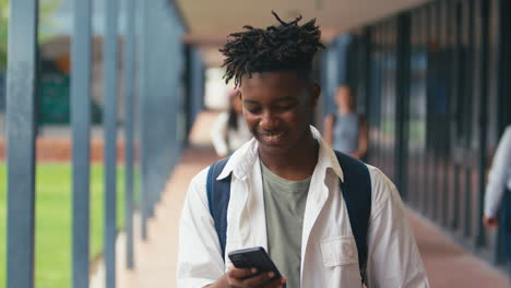 male high school or secondary student looking at social media or internet on phone outdoors