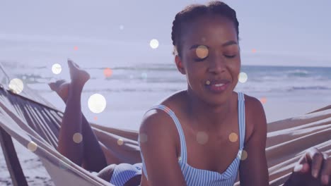 Animation-of-lens-flares-over-african-american-woman-relaxing-and-lying-on-hammock-at-beach