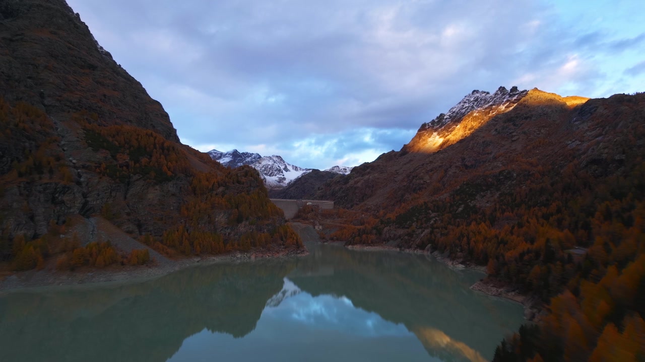 Vista aerea di un lago alpino e di una foresta autunnale che riflettono le montagne sotto un cielo serale. Ripresa aerea con avanzamento.