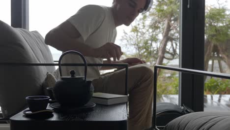 Man-Leaves-After-Reading-Book-On-Chair-With-Teapot-On-Side-Table