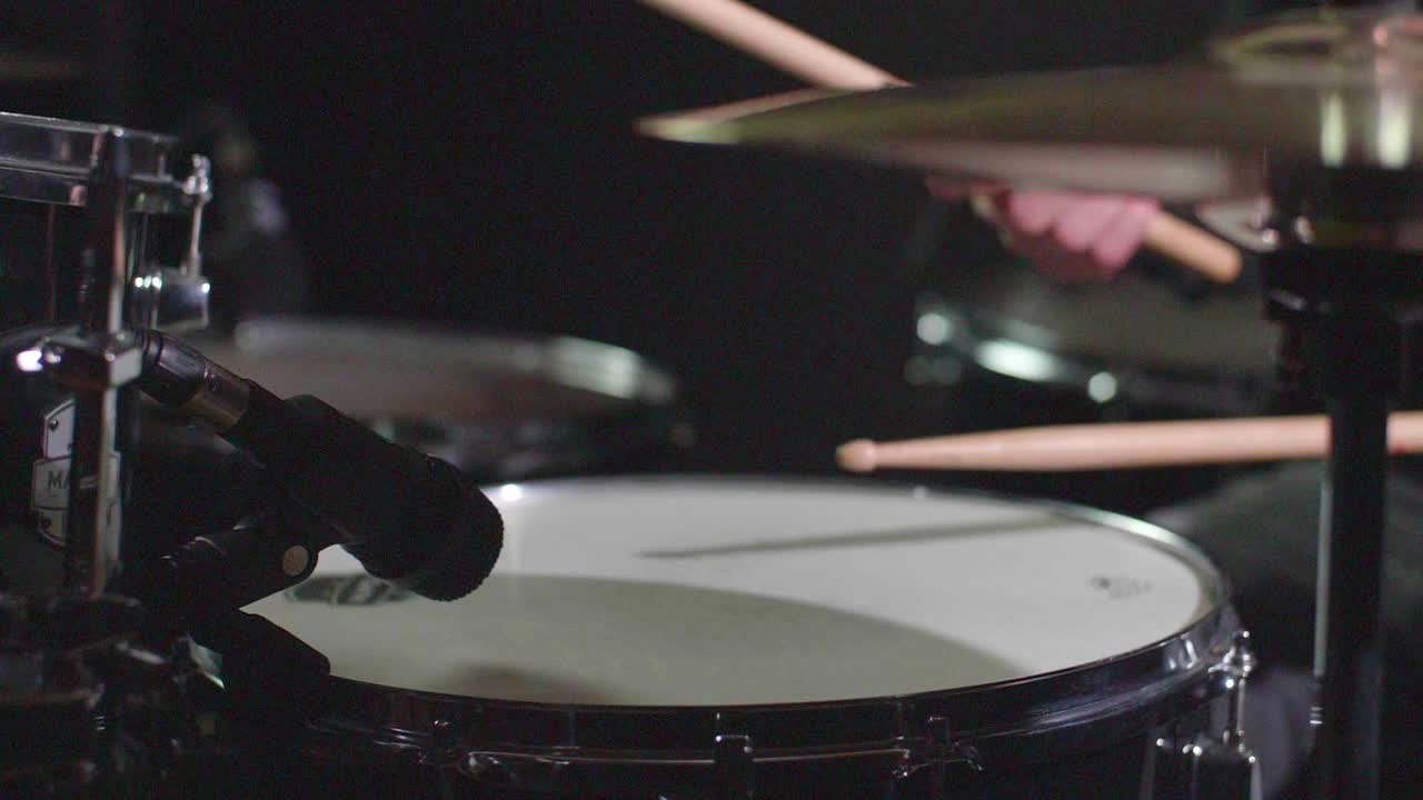 Smooth slow motion of a drum set being played in front of a dark background while camera makes a panning gimbal movement. Shallow depth. Shot in 4K
