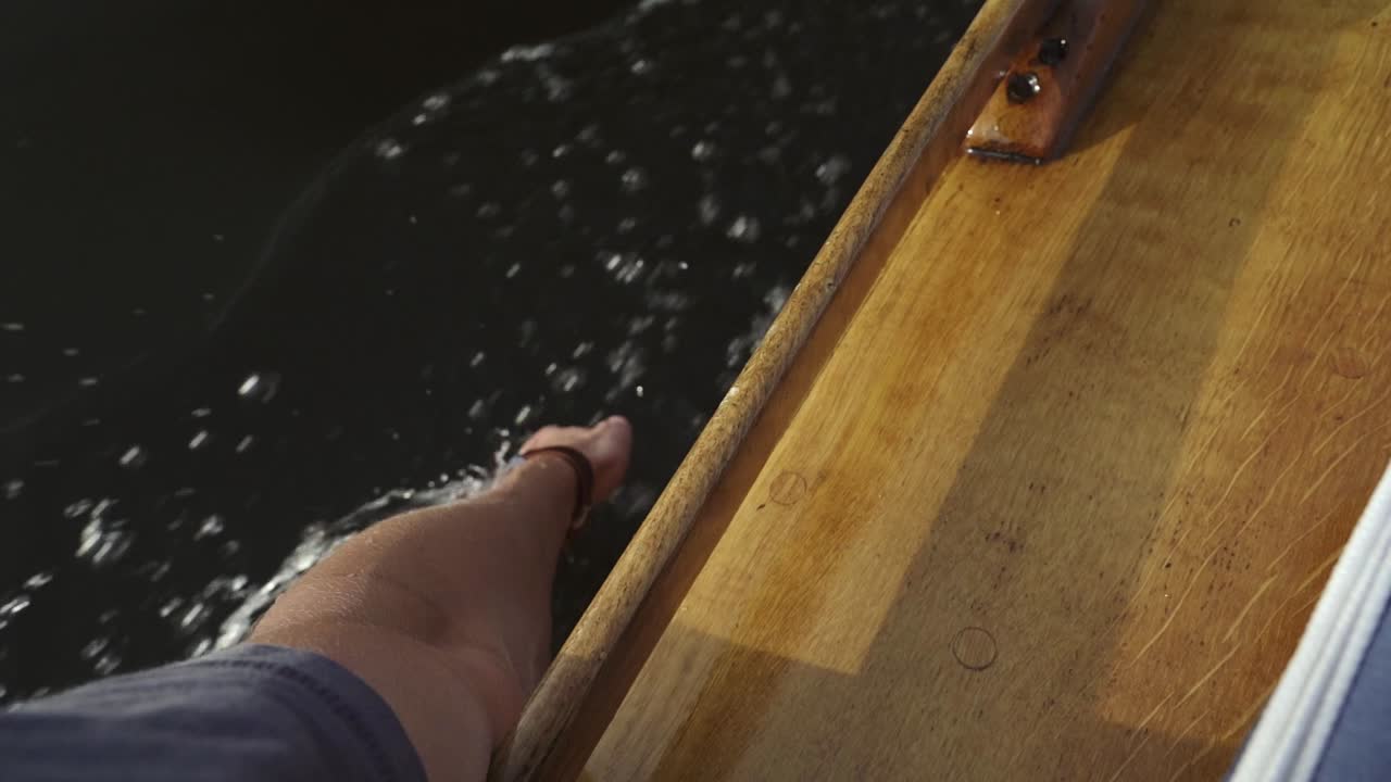 Hand with watch touches water during summer ride in old wooden boat in slow motion