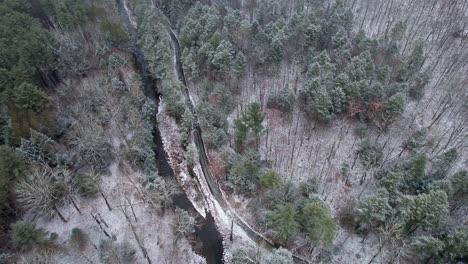 Aerial-drone-video-footage-of-a-snowy-pine-forest,-stream,-and-a-quiet-country-road-in-the-appalachian-mountains-during-winter