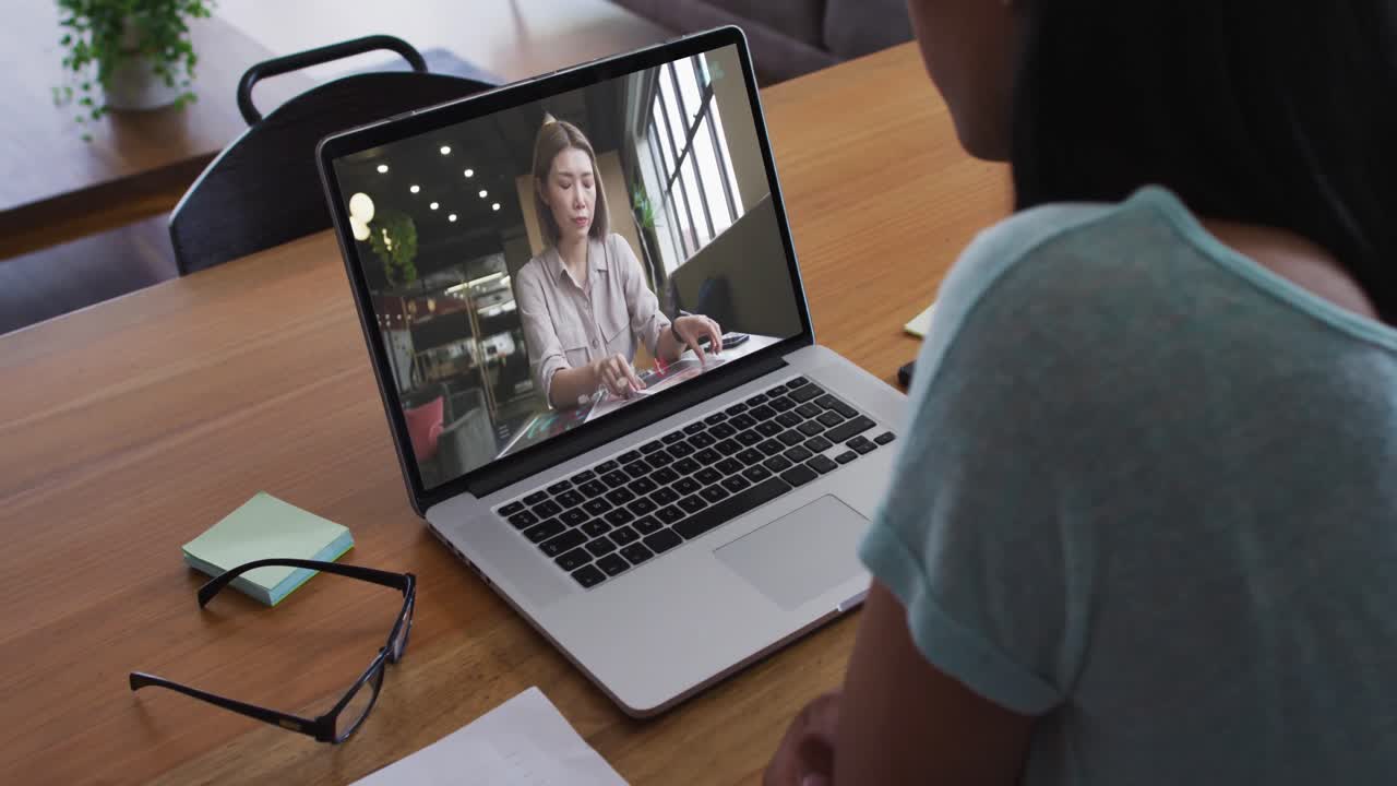 Mixed race businesswoman sitting at desk using laptop having video call with female colleague