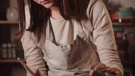 young woman potter making edges on the wet pot using a tool