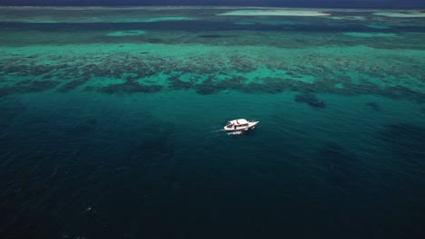 vista aérea de un pequeño bote blanco que navega lentamente en el océano índico azul turquesa profundo y cristalino en maldivas con turistas durante un safari en barco en busca de peces