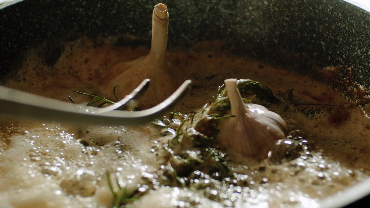 Stirring garlic bulbs and rosemary in sizzling hot molten butter for flavor
