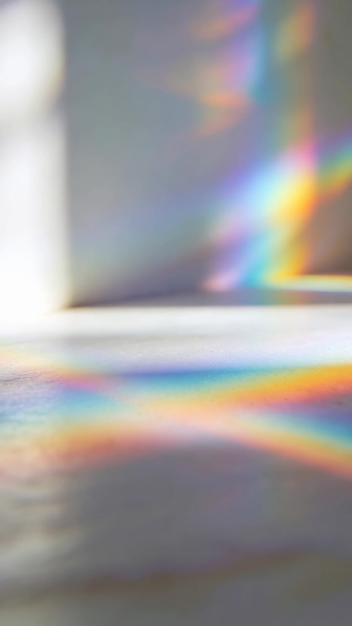 Video verticale: Bande arcobaleno cangianti che scivolano sul tavolo e salgono sul muro mentre il sole passa attraverso un prisma.