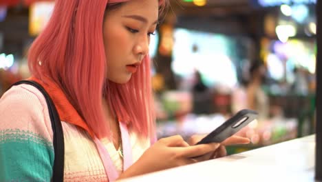 a young woman with pink hair engrossed in her smartphone, capturing the moment in a vibrant, colorful setting full of lights and background activity